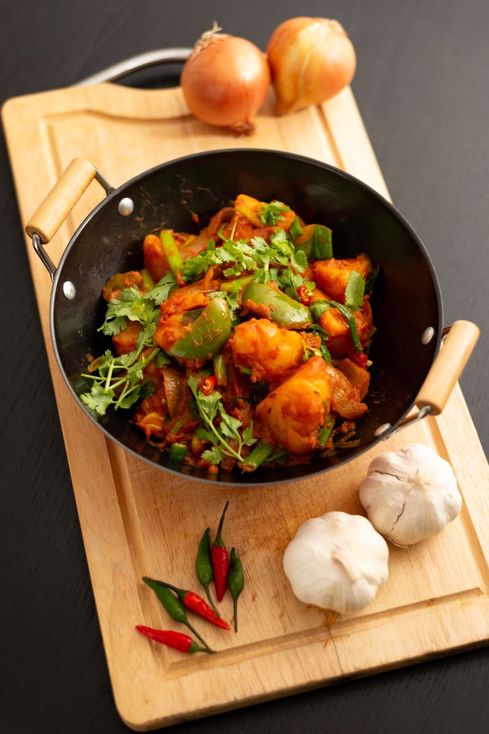 Delicious vegetable stir fry in a wok with fresh herbs and spices on a wooden board.