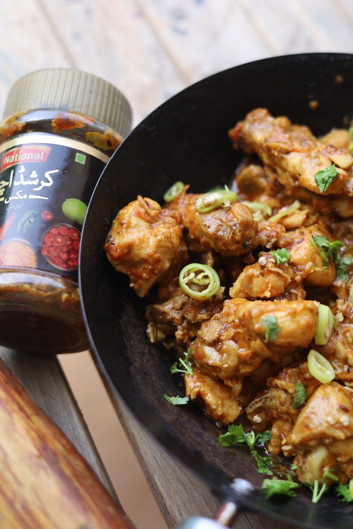 Delicious spicy chicken dish in a pan with seasoning jar on wooden table.