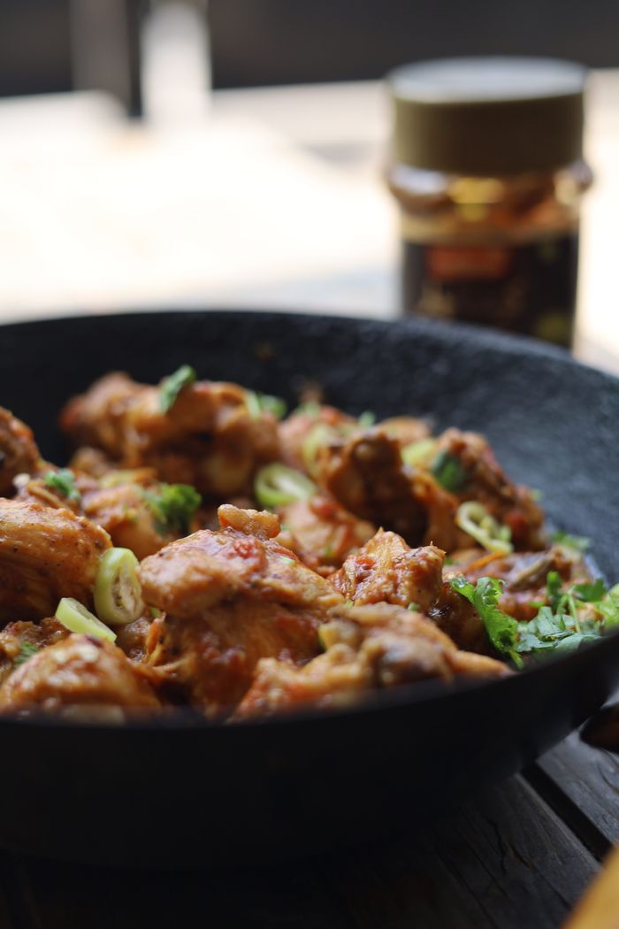 Close-up of flavorful chicken chunks in a black iron skillet with garnishes.