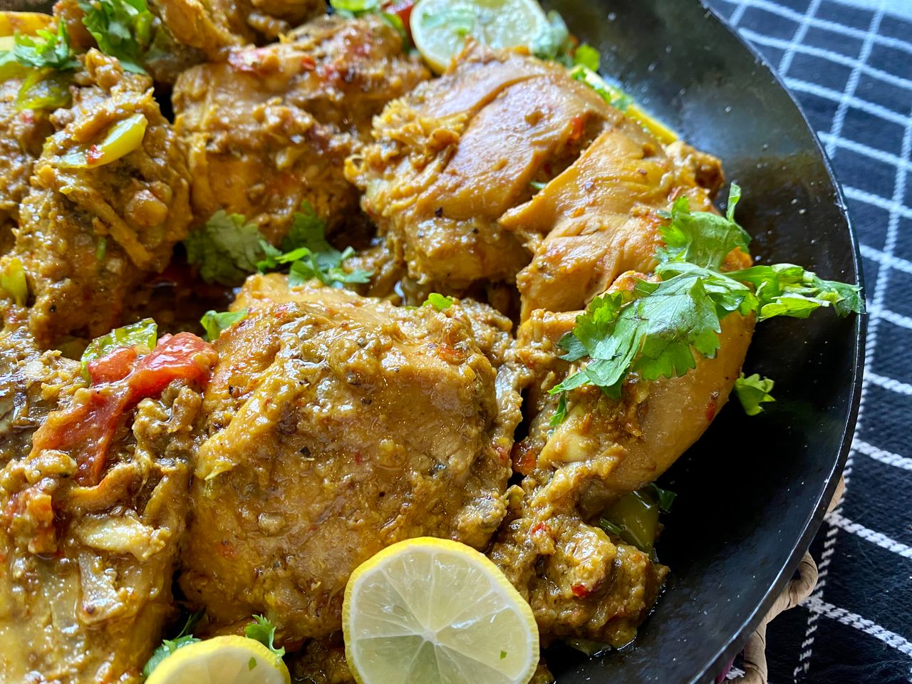 Close-up of a flavorful spiced chicken dish garnished with lemon slices and fresh herbs.